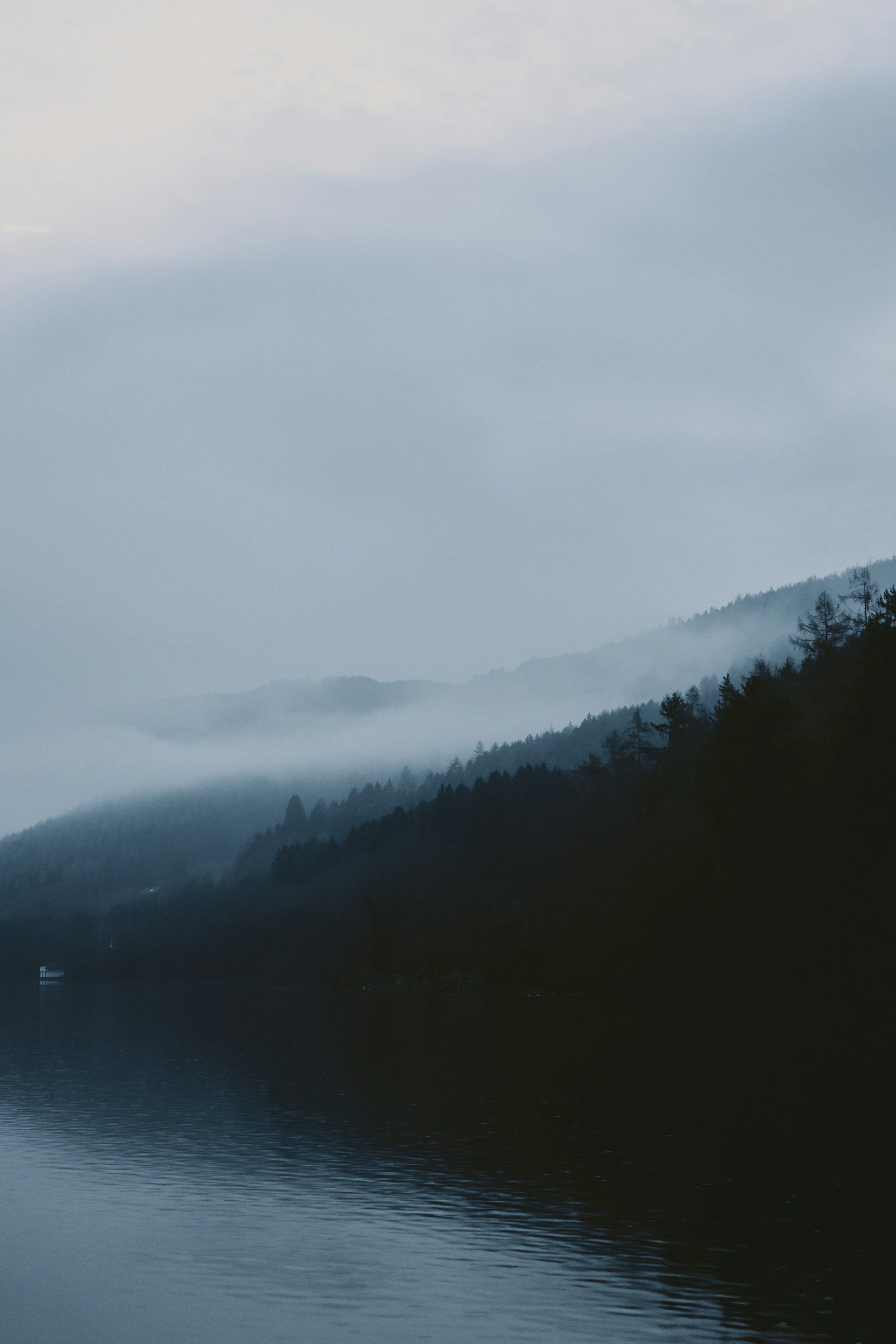 Misty mountain lake at dawn with house on distant shore