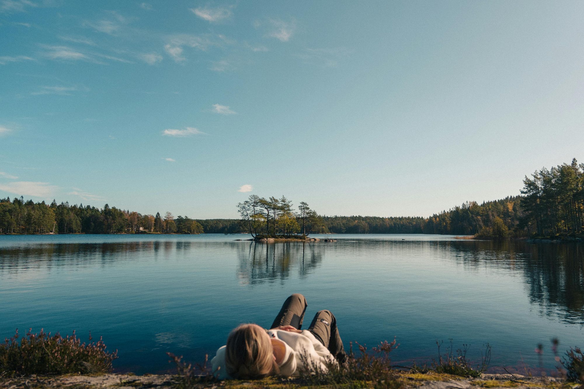 Person relaxing by a Nordic lake, island with pine trees in the distance